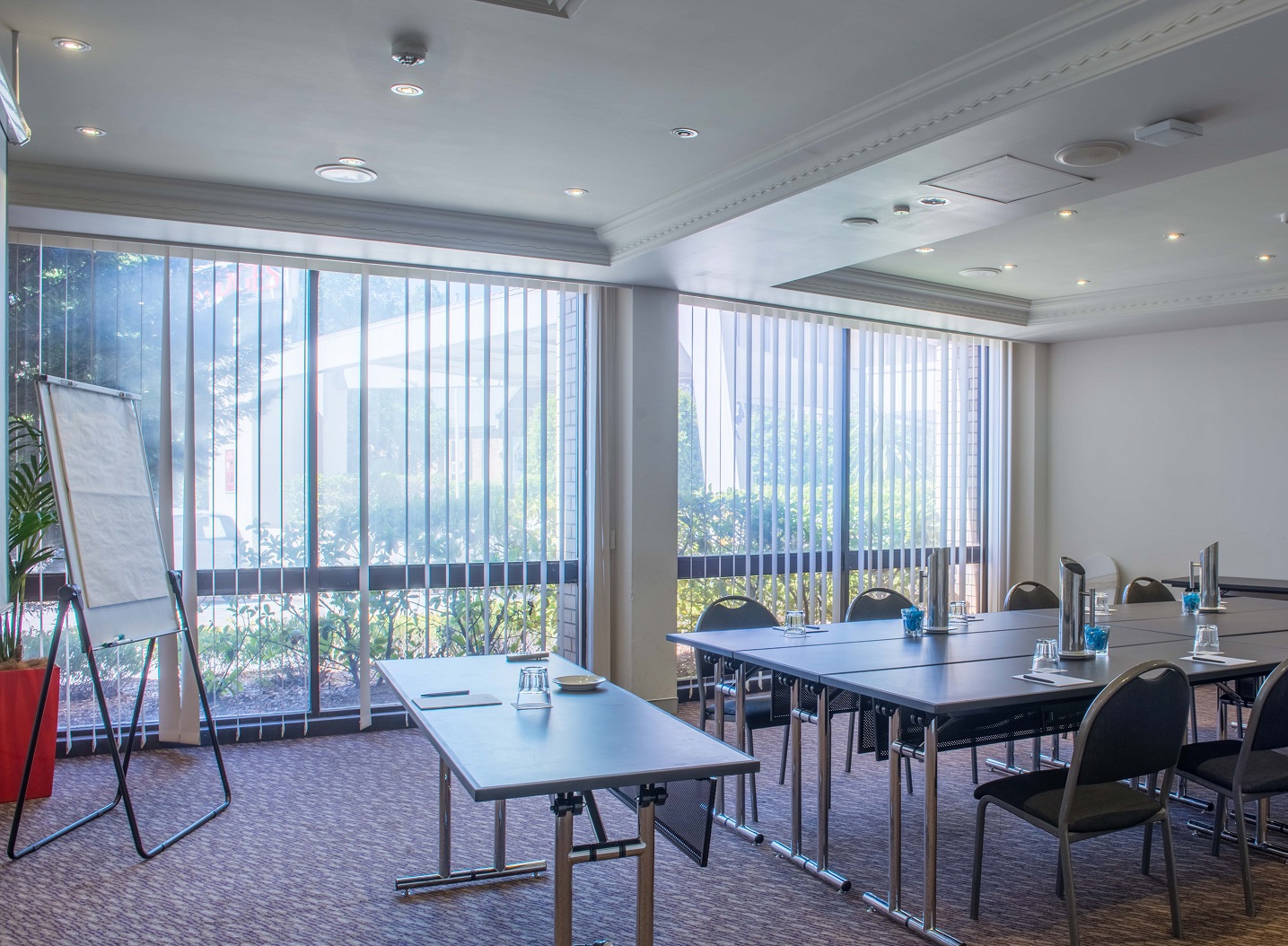 Bright conference room with floor-to-ceiling windows, rows of tables and chairs, and an easel near the glass wall.