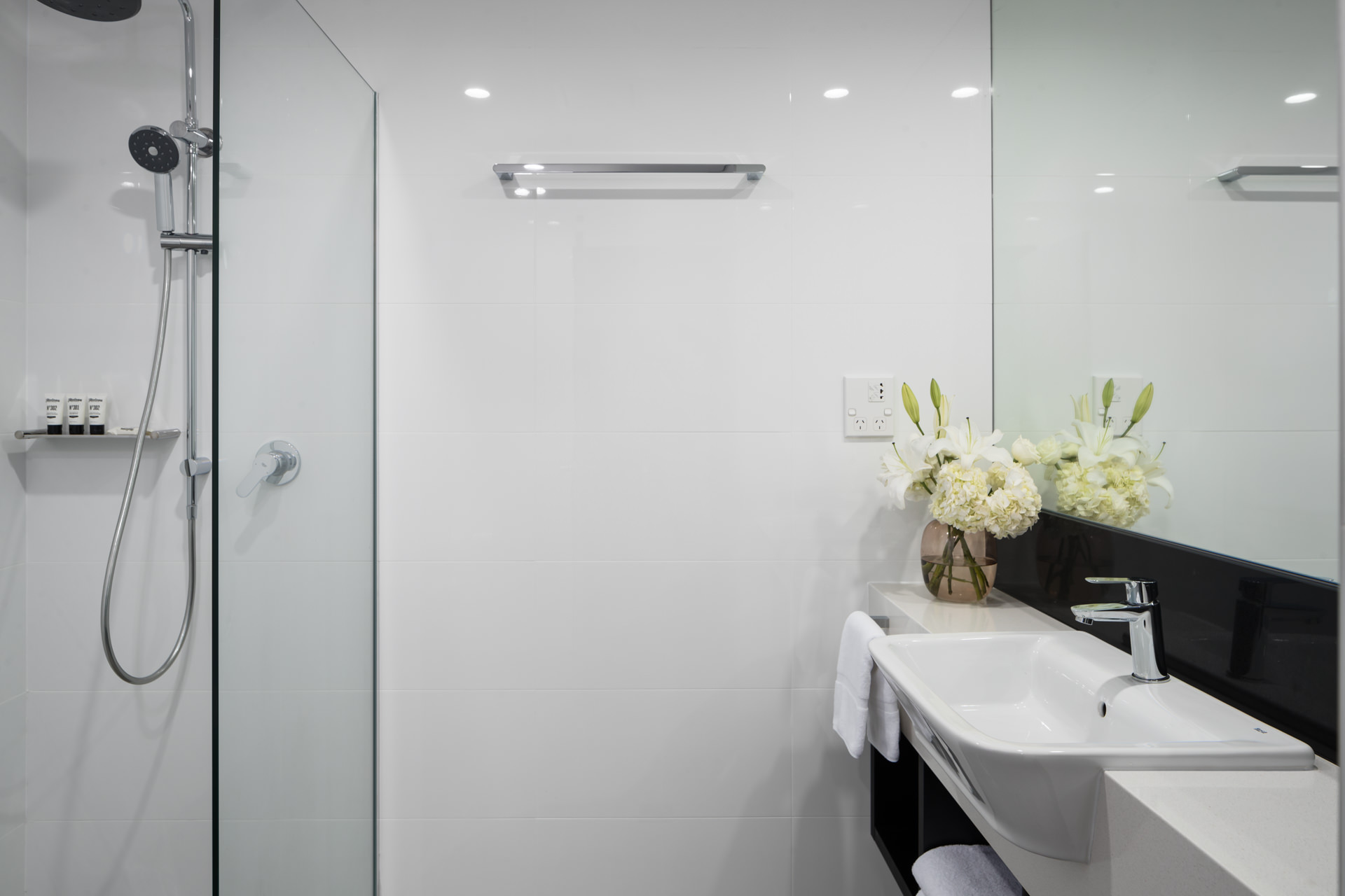 Modern bathroom with a glass-enclosed shower, white sink vanity, and flowers on the counter.