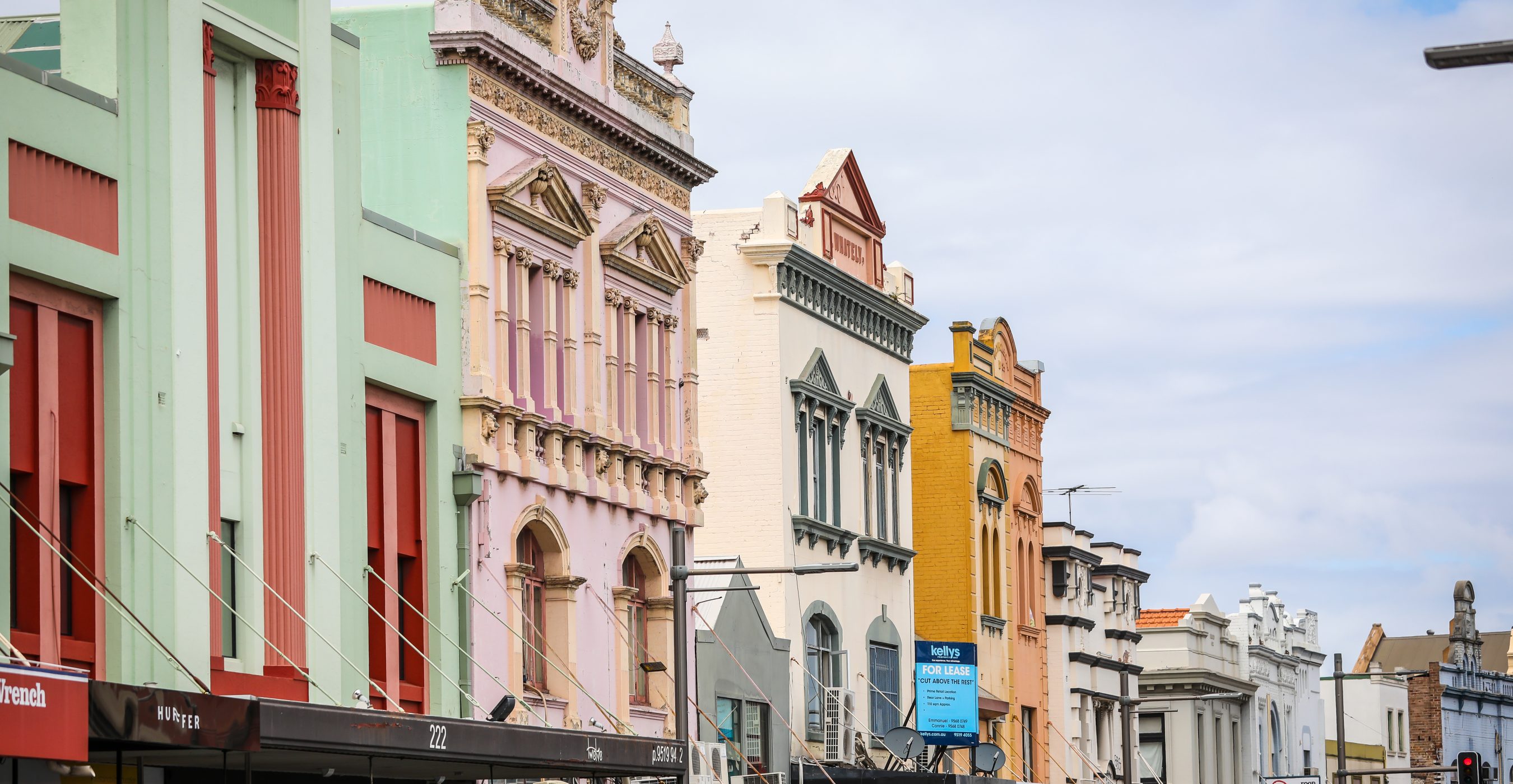 A row of colorful, ornate shopfronts lines a city street beneath a cloudy sky.