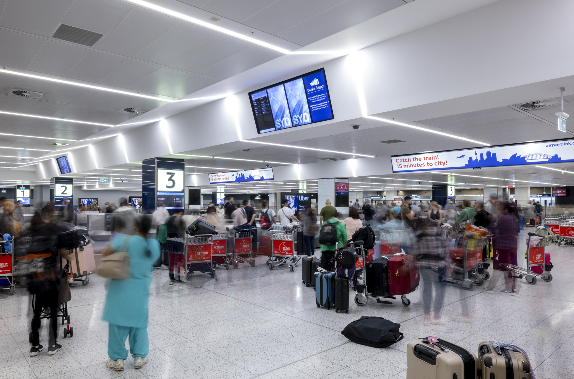 Travelers queue at airport check-in counters with suitcases beneath overhead flight information screens.