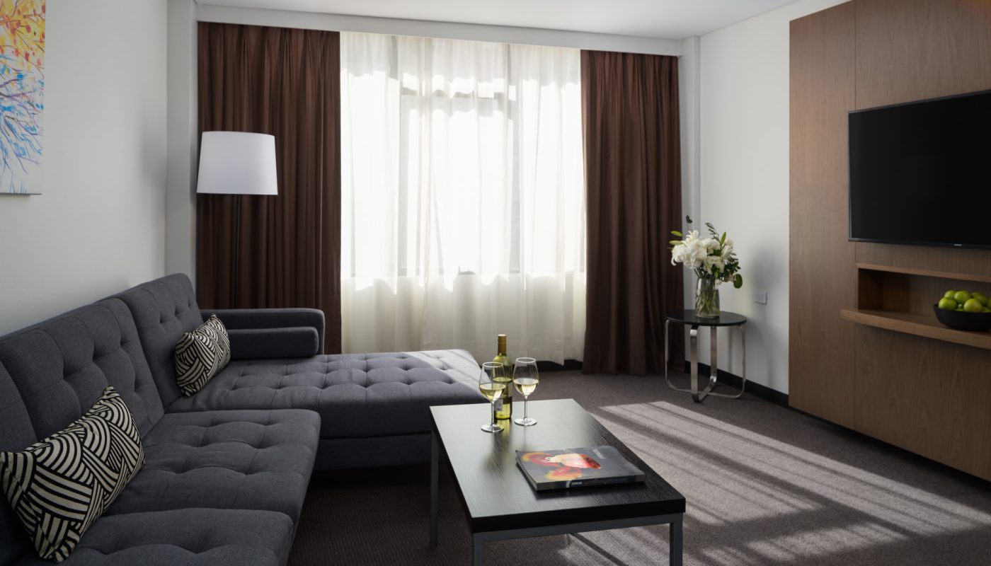Modern living room with a gray sectional sofa, black coffee table, floor lamp, sheer curtains, and wall-mounted TV.