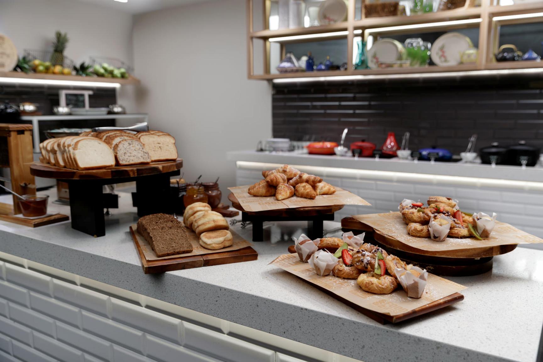 A bakery counter displays loaves of bread, pastries, and rolls on wooden boards and trays.