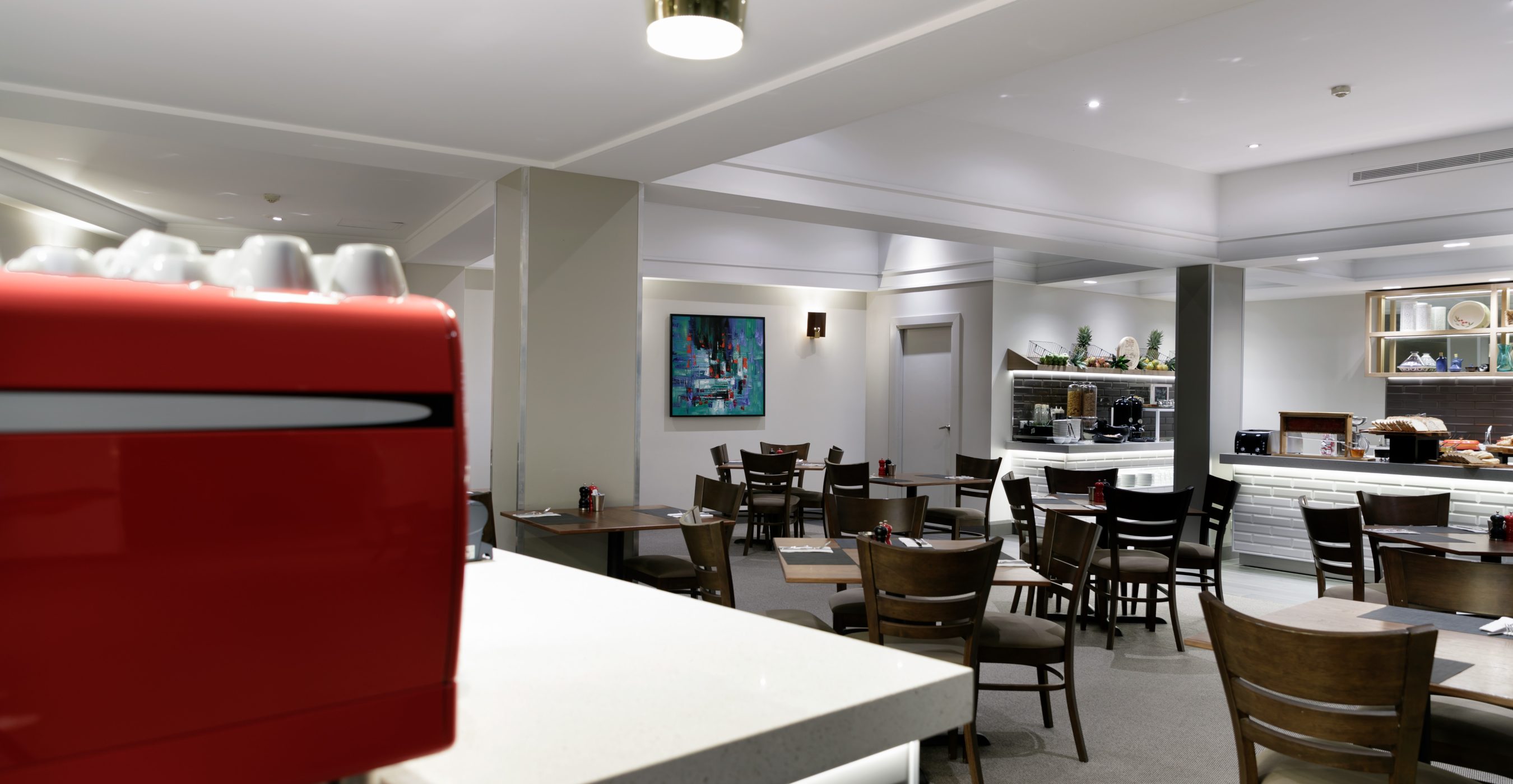 Modern restaurant dining area with dark tables and chairs, a service counter, wall art, and a blurred red object in the foreground.