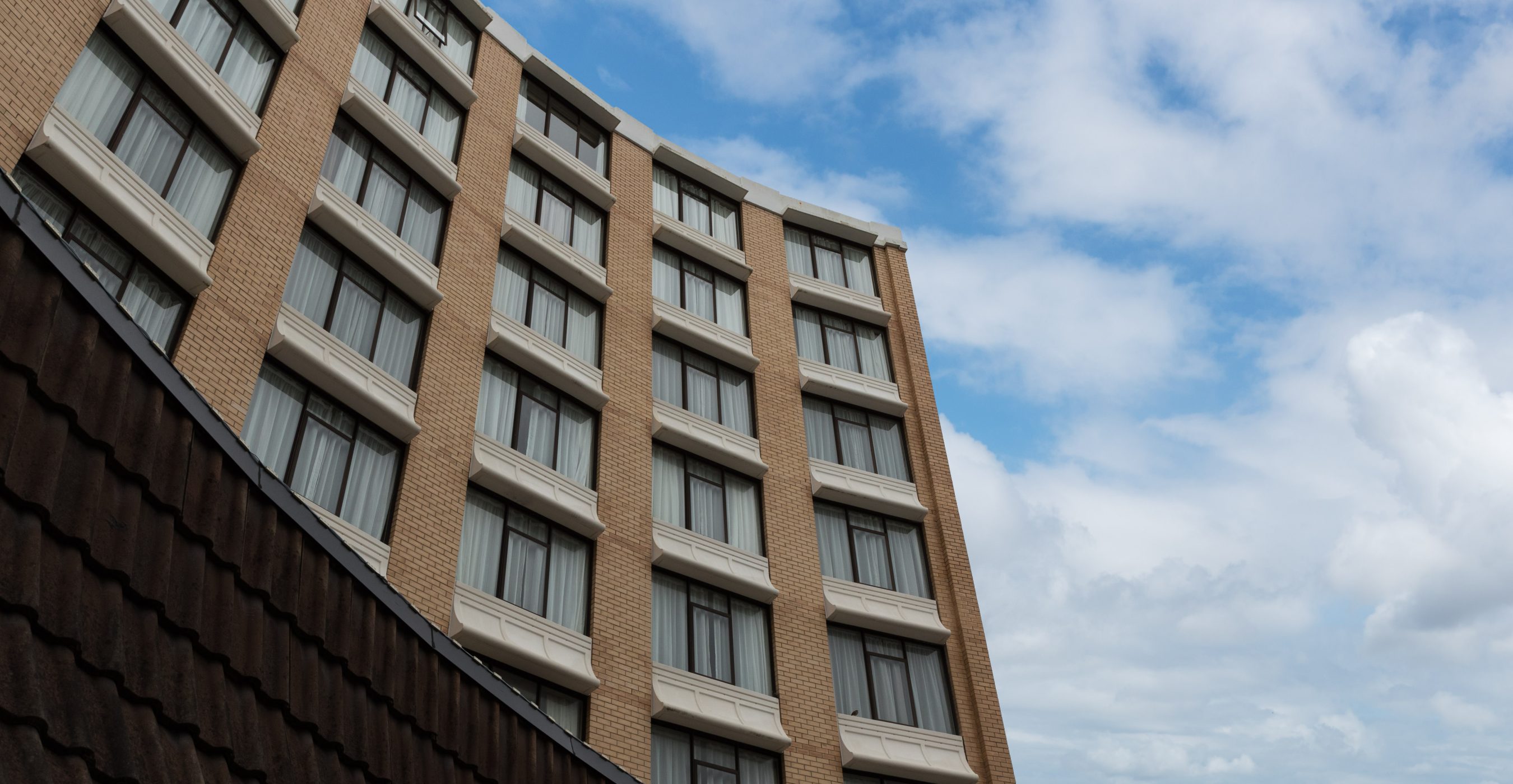 Low-angle view of a multi-story building with rows of windows against a partly cloudy blue sky.
