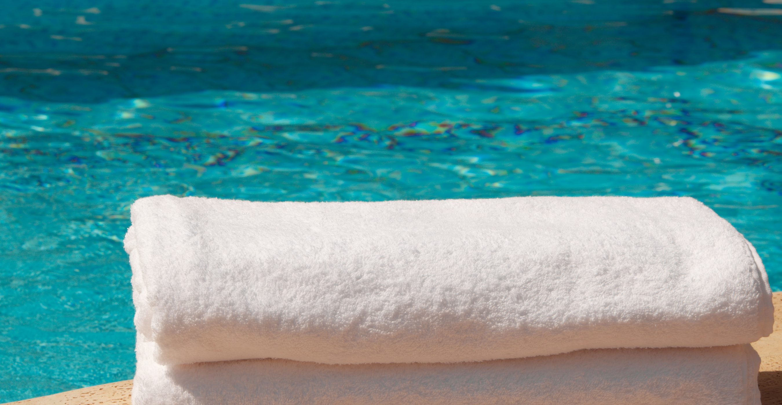 Two folded white towels rest on a ledge beside a turquoise swimming pool.