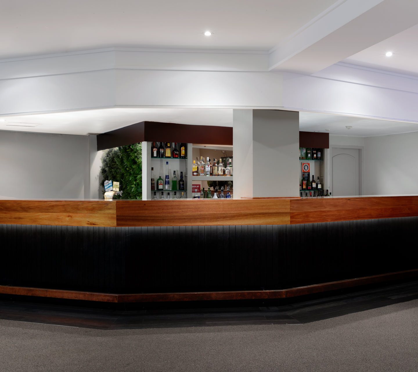 A long dark bar with wood trim sits beneath liquor shelves in a modern interior.