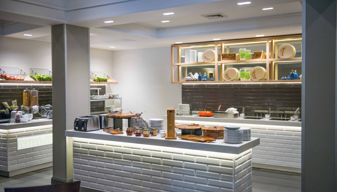 Modern kitchen with white tiled counters, a dark backsplash, and open shelves displaying dishes and cookware.