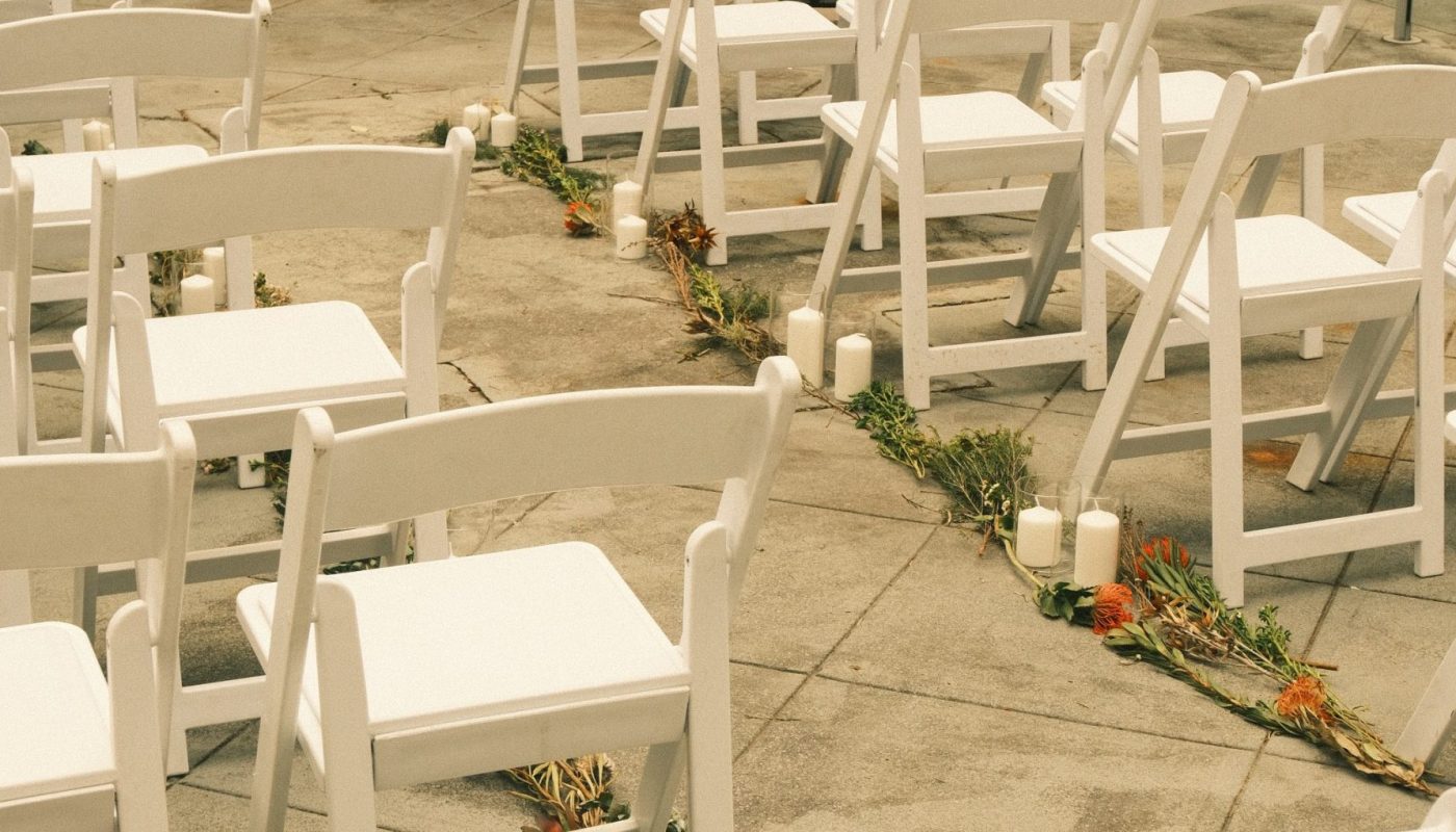 Rows of white folding chairs on a stone patio, with candles and flower arrangements lining the aisle.