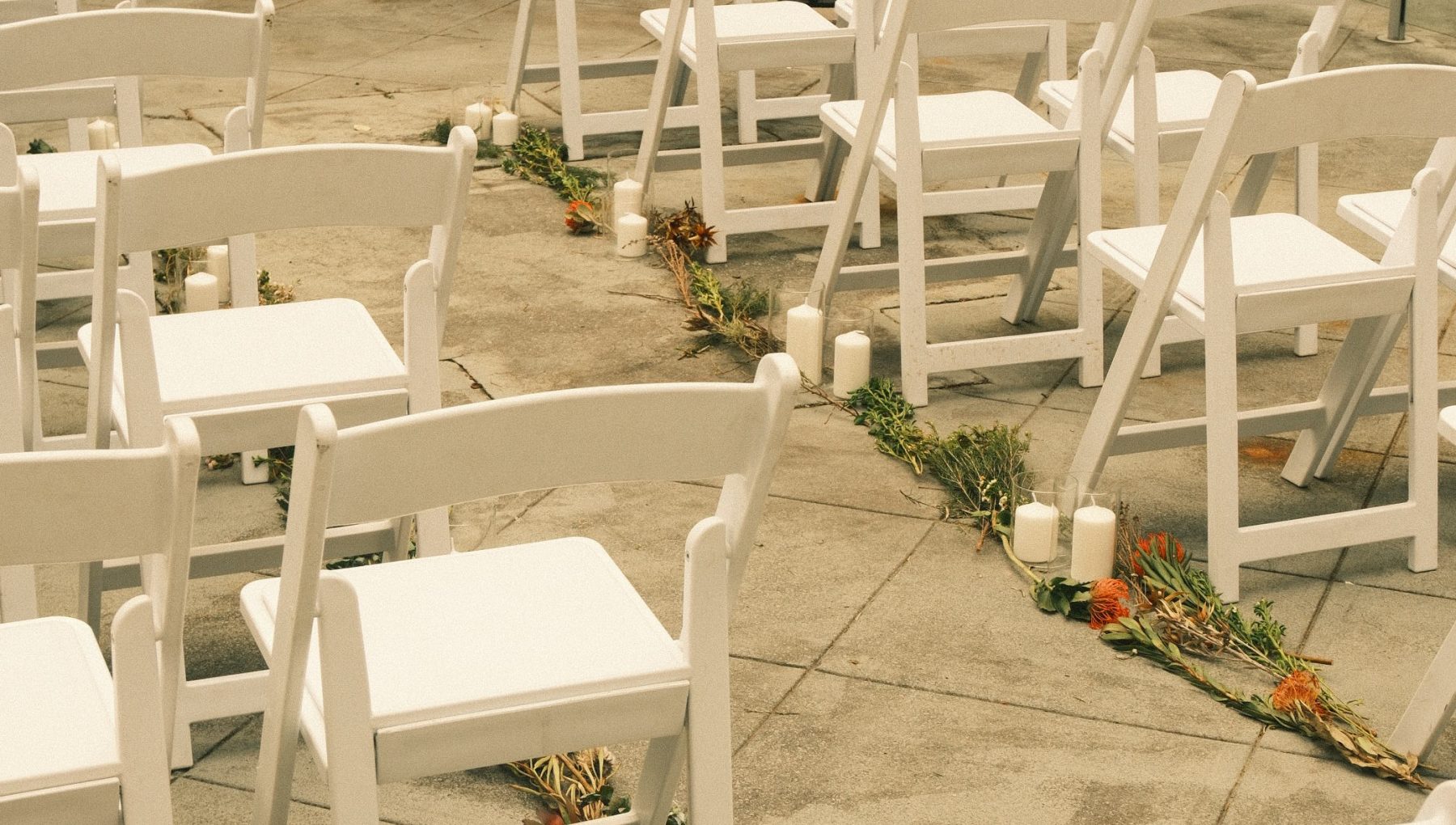 Rows of white folding chairs on a stone patio, with candles and flower arrangements lining the aisle.