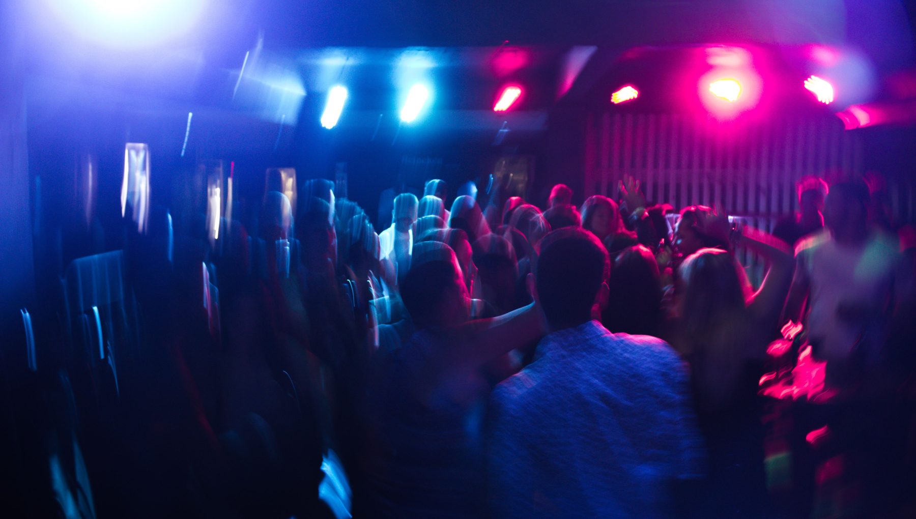 A motion-blurred crowd fills a dark venue beneath bright blue and magenta stage lights.